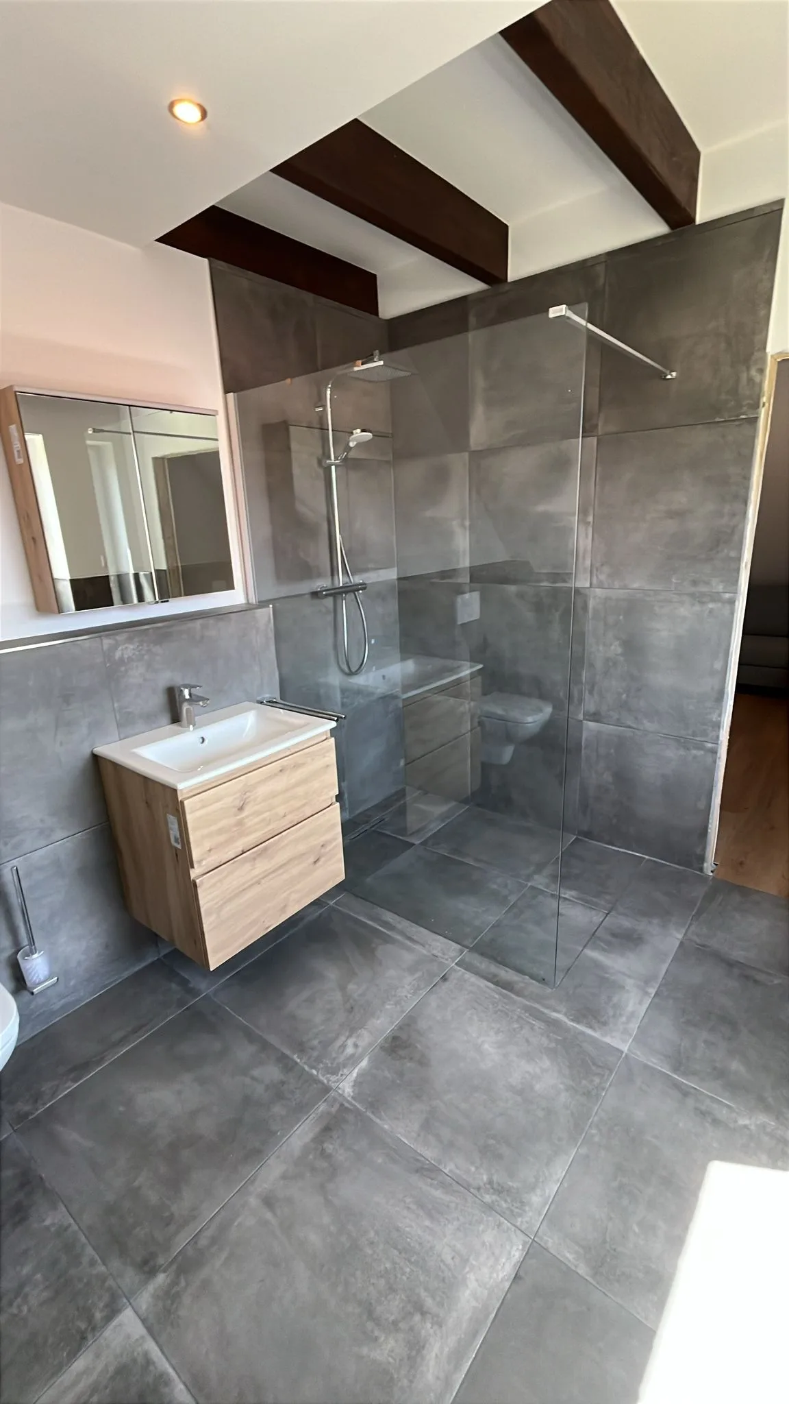 Modernes Badezimmer mit ebenerdiger Glasdusche, Regendusche und Waschtisch in Holzoptik.
